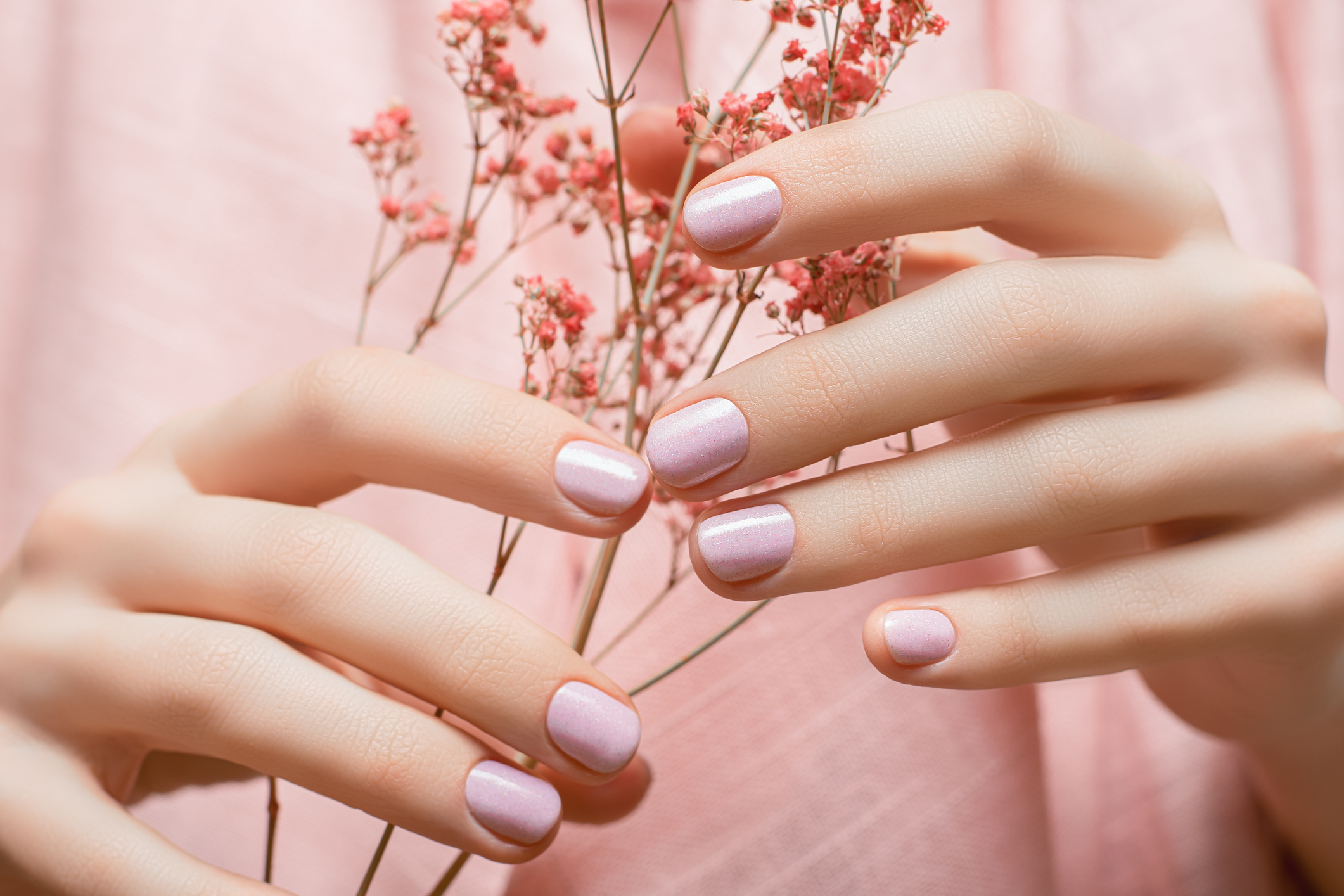 Female hands with pink nail design. Pink nail polish manicure. Woman hands hold orange flowers.