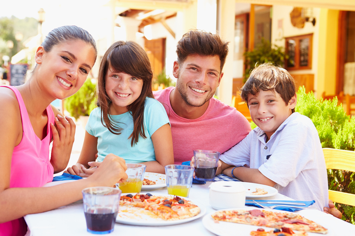 Family eating pizza at outdoor restaurant smiling for camera
