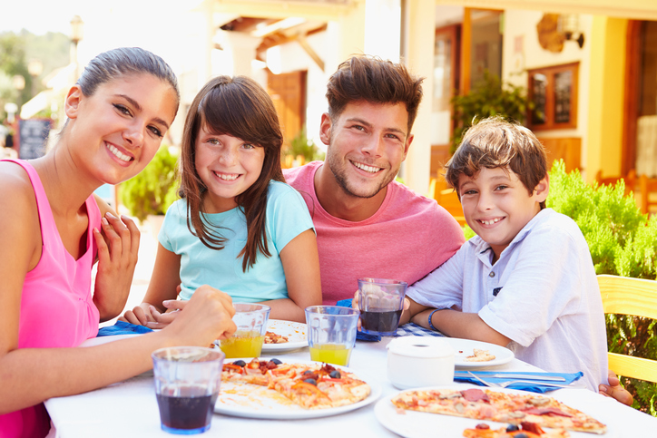 Family eating pizza at outdoor restaurant smiling for camera Family eating pizza at outdoor restaurant smiling for camera