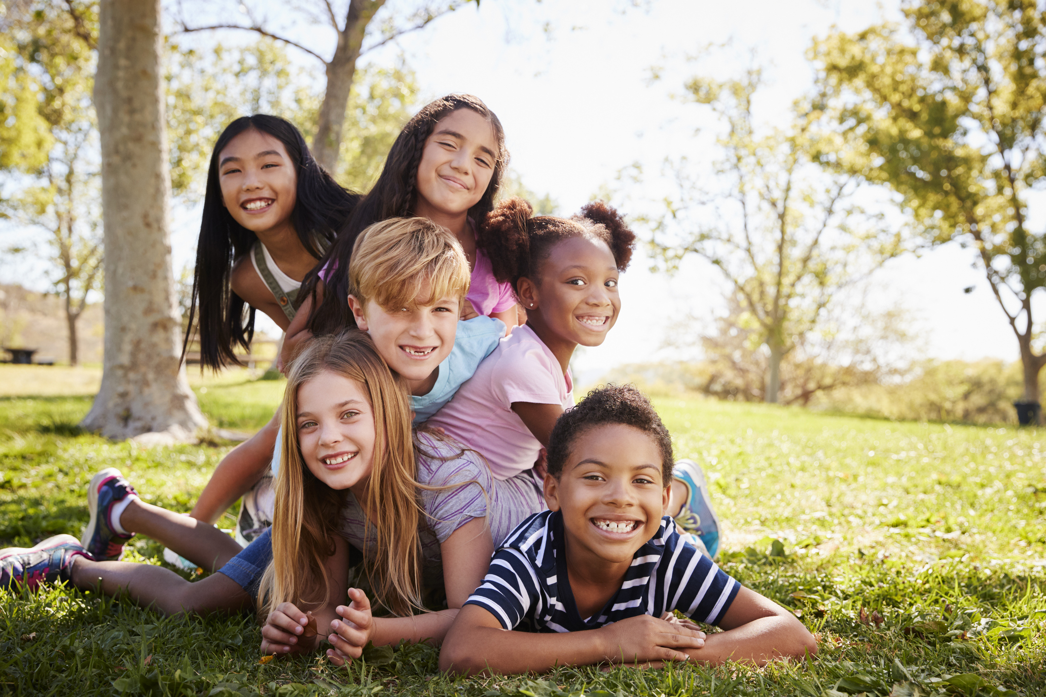 Multi-ethnic group of kids lying on each other in a park Multi-ethnic group of kids lying on each other in a park