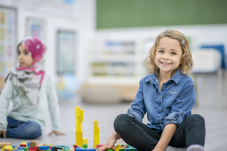 Little girl plays with toys while sitting on the ground