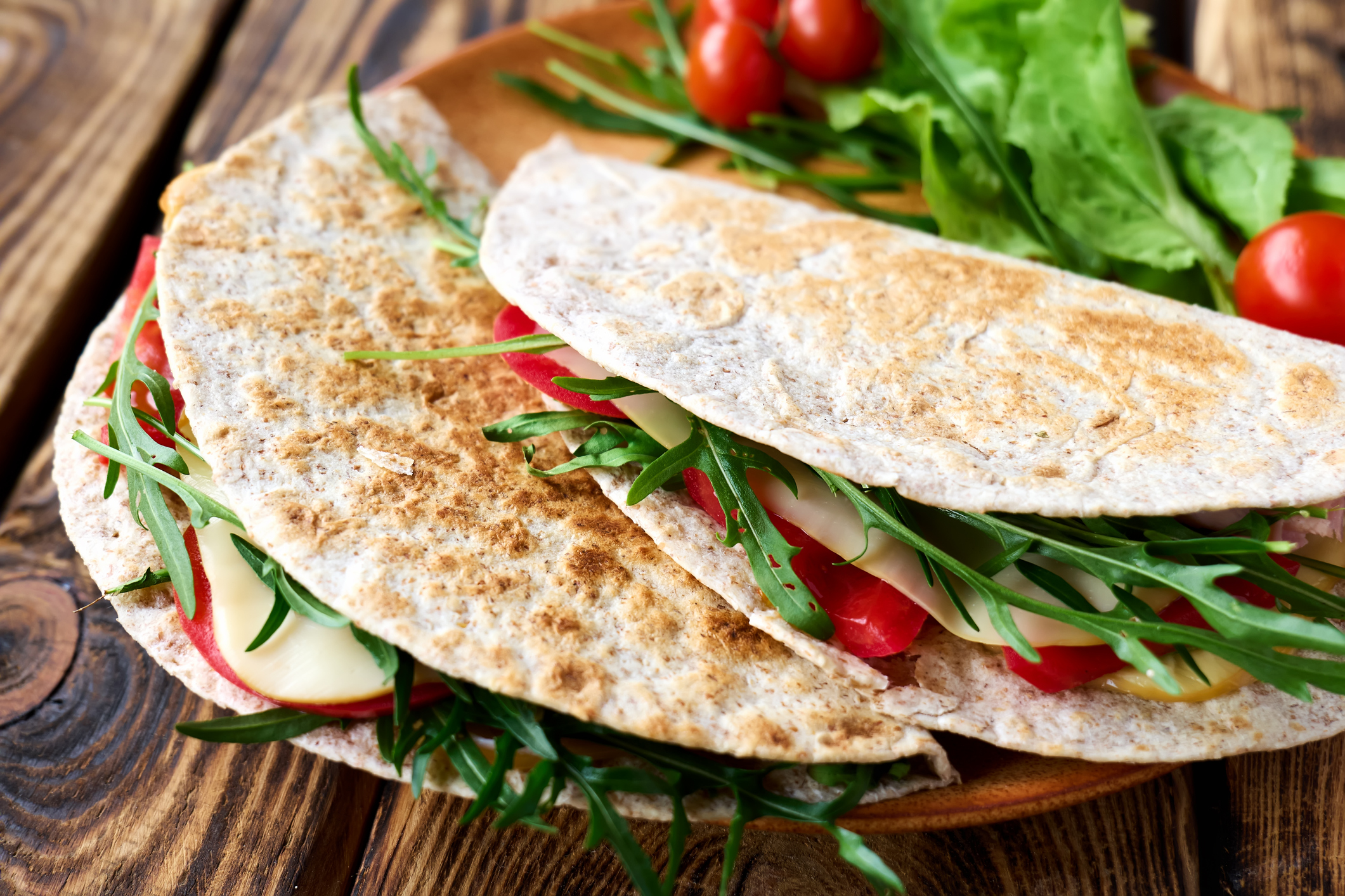 Piadina Romagnola with mozzarella cheese, tomatoes, ham and rocket salad on wooden table. Italian flatbread or open sandwich. Selective focus.